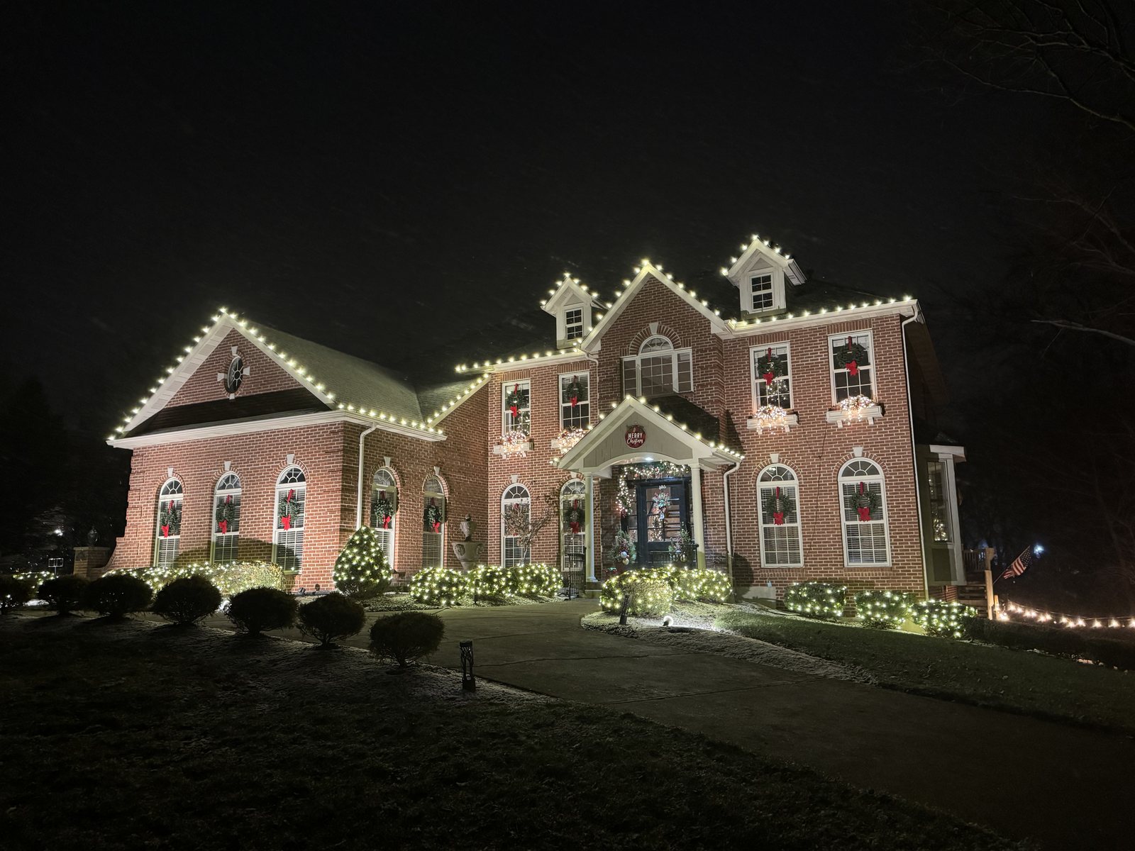 Warm white roofline, dormers and window wreaths on a brick colonial — holiday lighting by Shine in Cincinnati