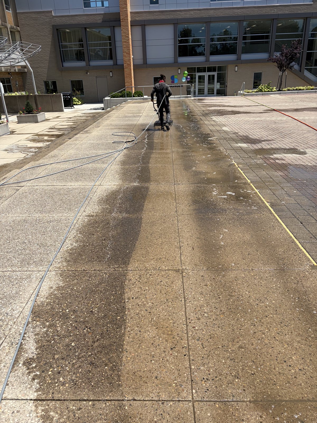 Surface cleaning a concrete plaza, clean line visible mid-pass — flat surface pressure washing by Shine
